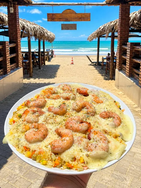 Prato de arroz com camarões gratinados, segurado de frente para a praia