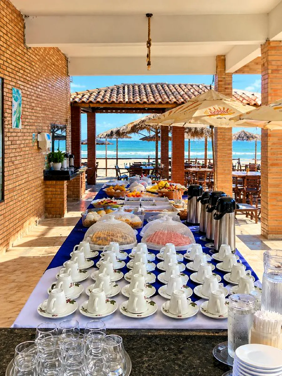 Mesa do café da manhã com xícaras, garrafas de café e a praia ao fundo