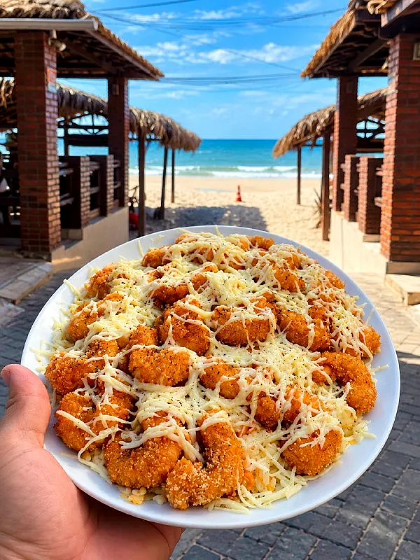 Camarões empanados com queijo, com as barracas de palha e o mar atrás
