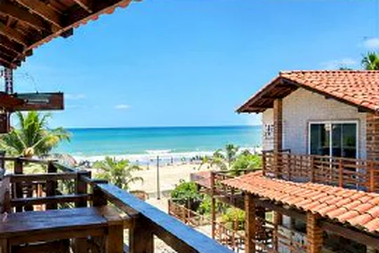 Vista da varanda para a praia, com telhados e coqueiros