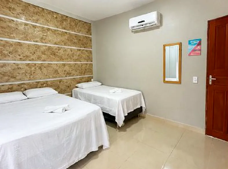 Quarto com cama de casal, cama de solteiro e parede de pedra
