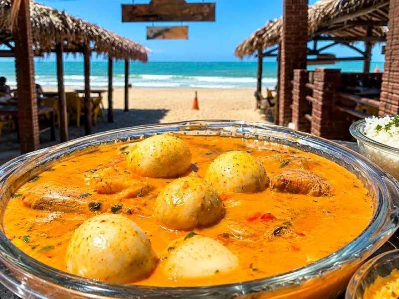 Peixada com ovos e molho dourado, com a praia ao fundo
